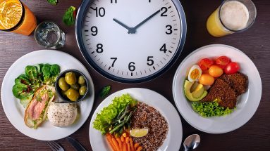 Ein gedeckter Tisch mit drei Mahlzeiten und einer Uhr, die den richtigen Essensrhythmus symbolisieren.