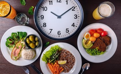 Ein gedeckter Tisch mit drei Mahlzeiten und einer Uhr, die den richtigen Essensrhythmus symbolisieren.
