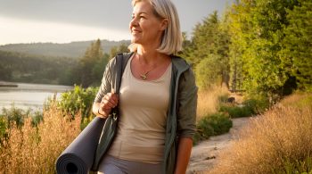 Frau Mitte 40 mit Yogamatte, entspannt beim Spaziergang in der Natur, symbolisiert Balance und Gesundheit in den Wechseljahren.