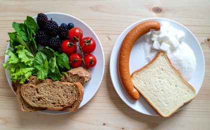 Eine Gegenüberstellung von zwei Tellern: Links Fast Food (Zucker, weißes Brot, Wurst), rechts frische Lebensmittel wie Beeren, Vollkornbrot und grünes Gemüse.
