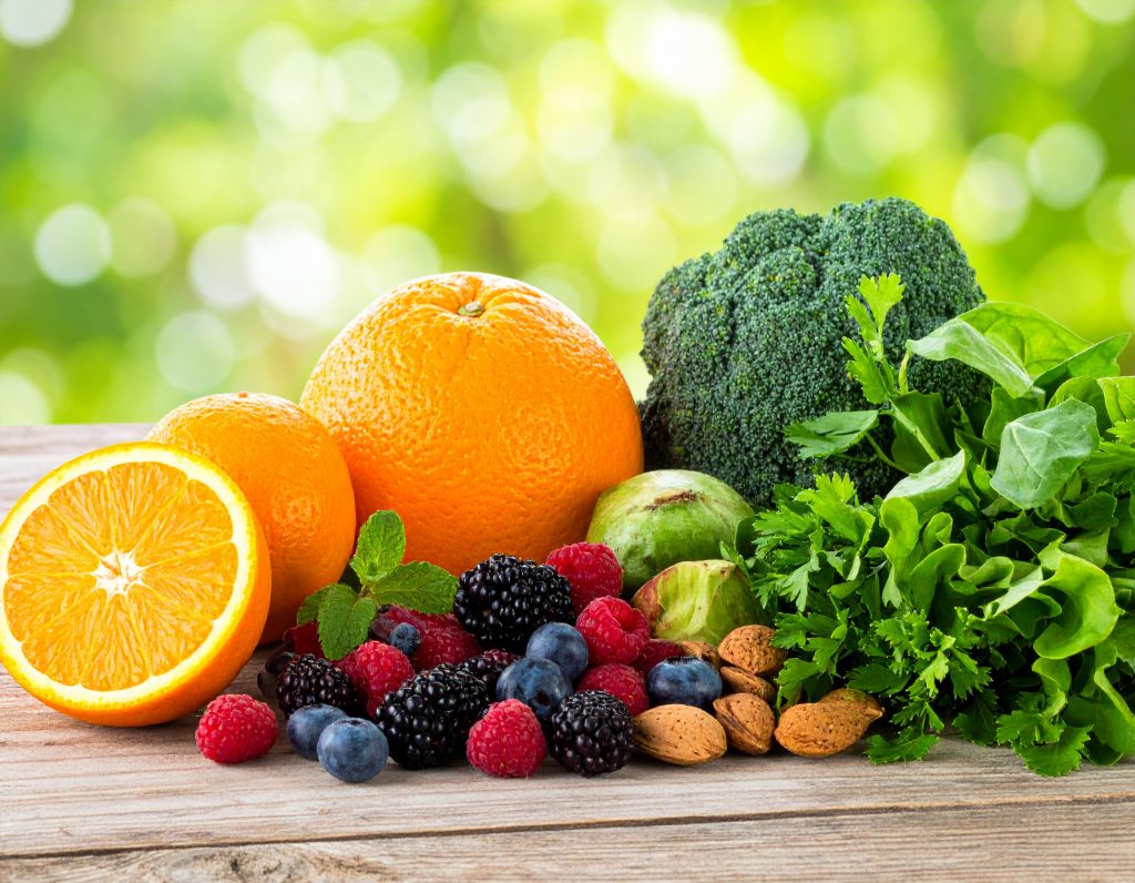 Ein Bild von frischem Obst, Gemüse und Nüssen – wie Orangen, Beeren, Mandeln und grünem Gemüse – in einer natürlichen, hellen Umgebung, die den Fokus auf natürliche Vitalstoffe unterstreicht.