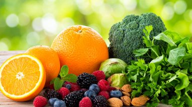 Ein Bild von frischem Obst, Gemüse und Nüssen – wie Orangen, Beeren, Mandeln und grünem Gemüse – in einer natürlichen, hellen Umgebung, die den Fokus auf natürliche Vitalstoffe unterstreicht.