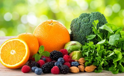 Ein Bild von frischem Obst, Gemüse und Nüssen – wie Orangen, Beeren, Mandeln und grünem Gemüse – in einer natürlichen, hellen Umgebung, die den Fokus auf natürliche Vitalstoffe unterstreicht.